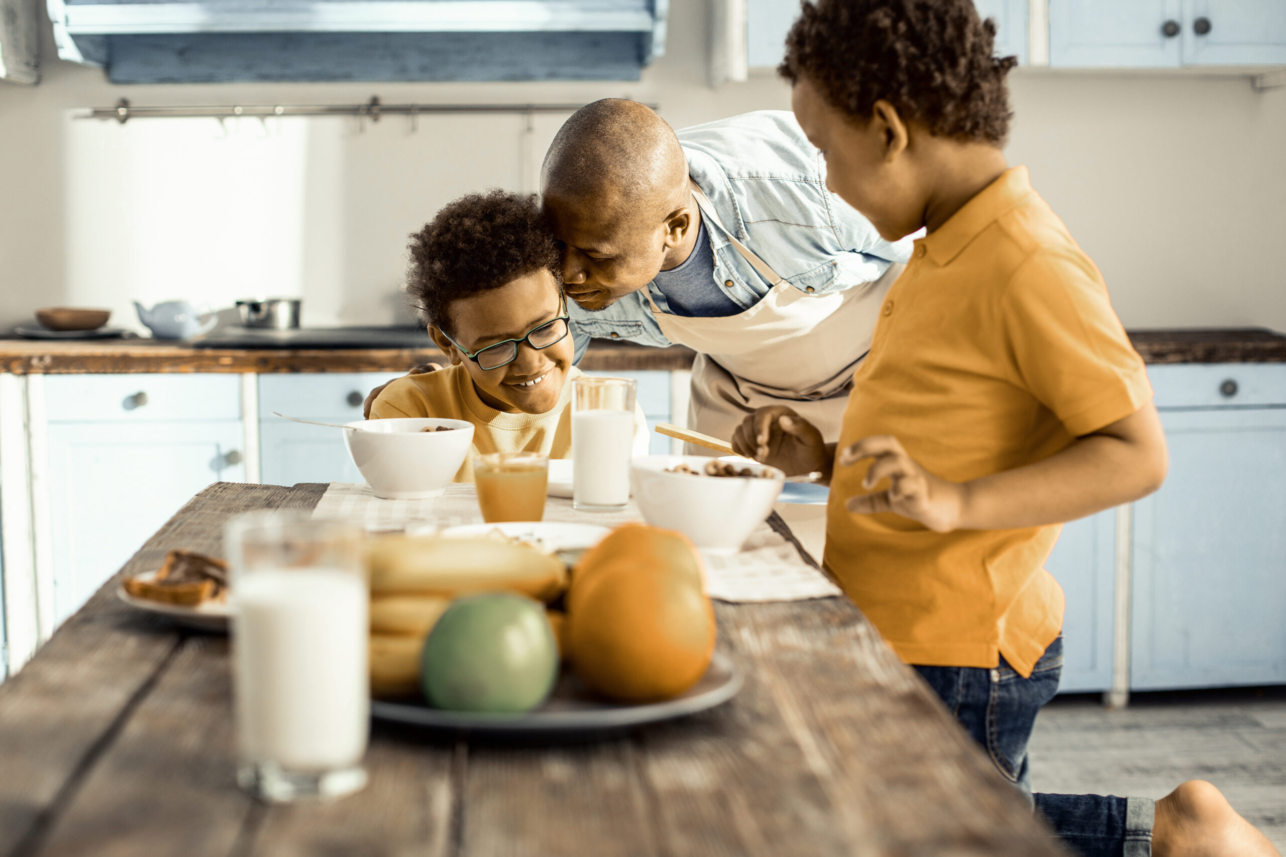Man in apron in turns hugging his sons.