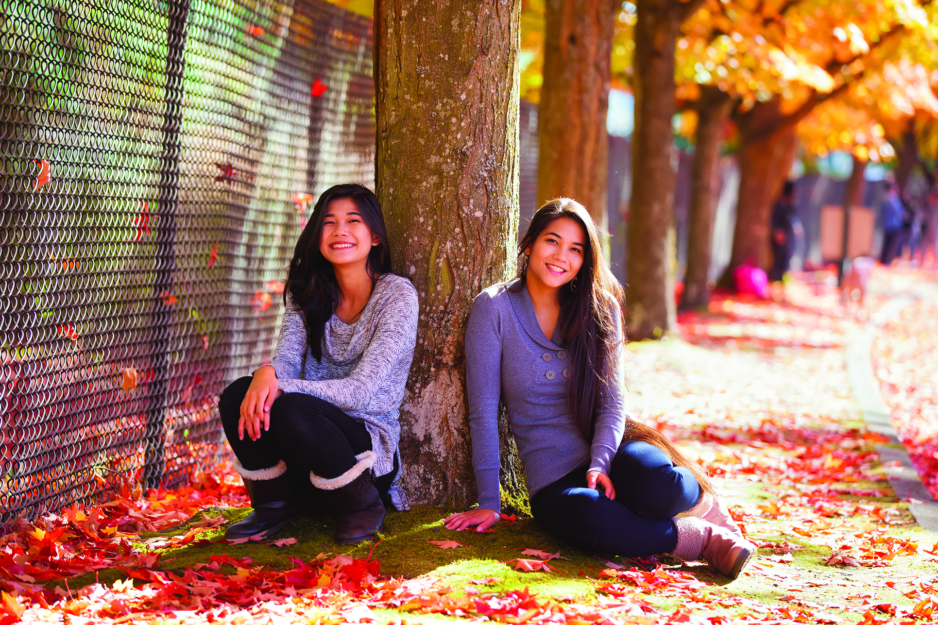 Biracial teen girl sitting under colorful maple trees in autumn