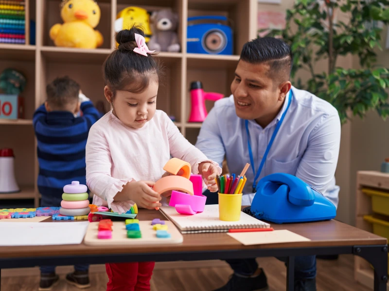 Hispanic teacher and a girl building blocks in the kindergarten