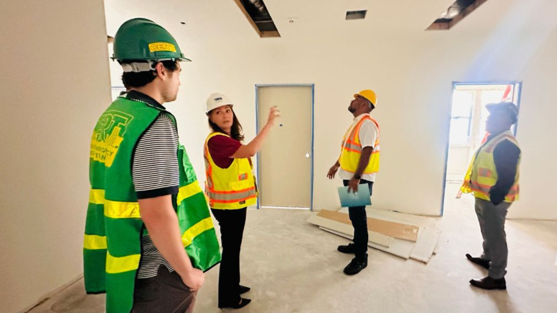 Staff in reflective vests and hard hats lead Soto-Martinez and Walker through a room under construction